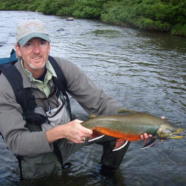Brian Snow kneeling in a stream holding a big trout with a red belly.
