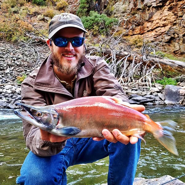 Mitchell Murphy holding a huge fish kneeling by a river.