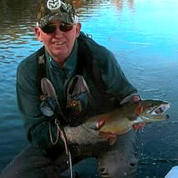 Pat Hooley kneeling in a stream with an impressive trout caught fly fishing.