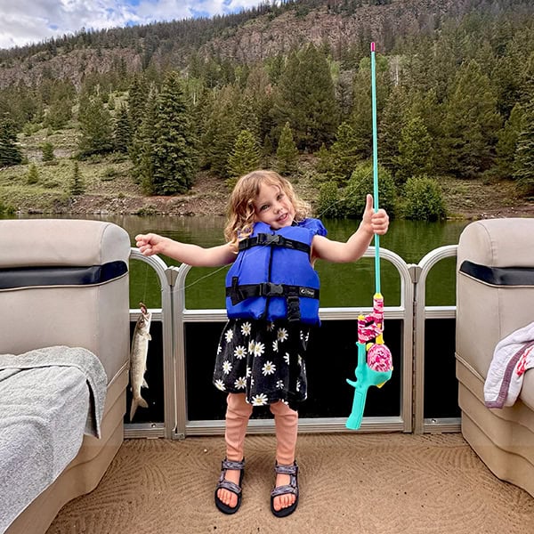 A young angler shows off her catch standing in Dan's Fly Shop's pontoon boat.