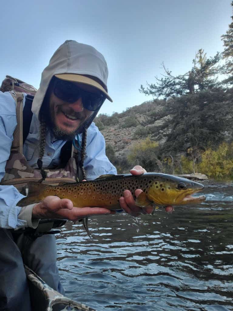 DFS guide holds a large golden and spotted trout beside a stream.