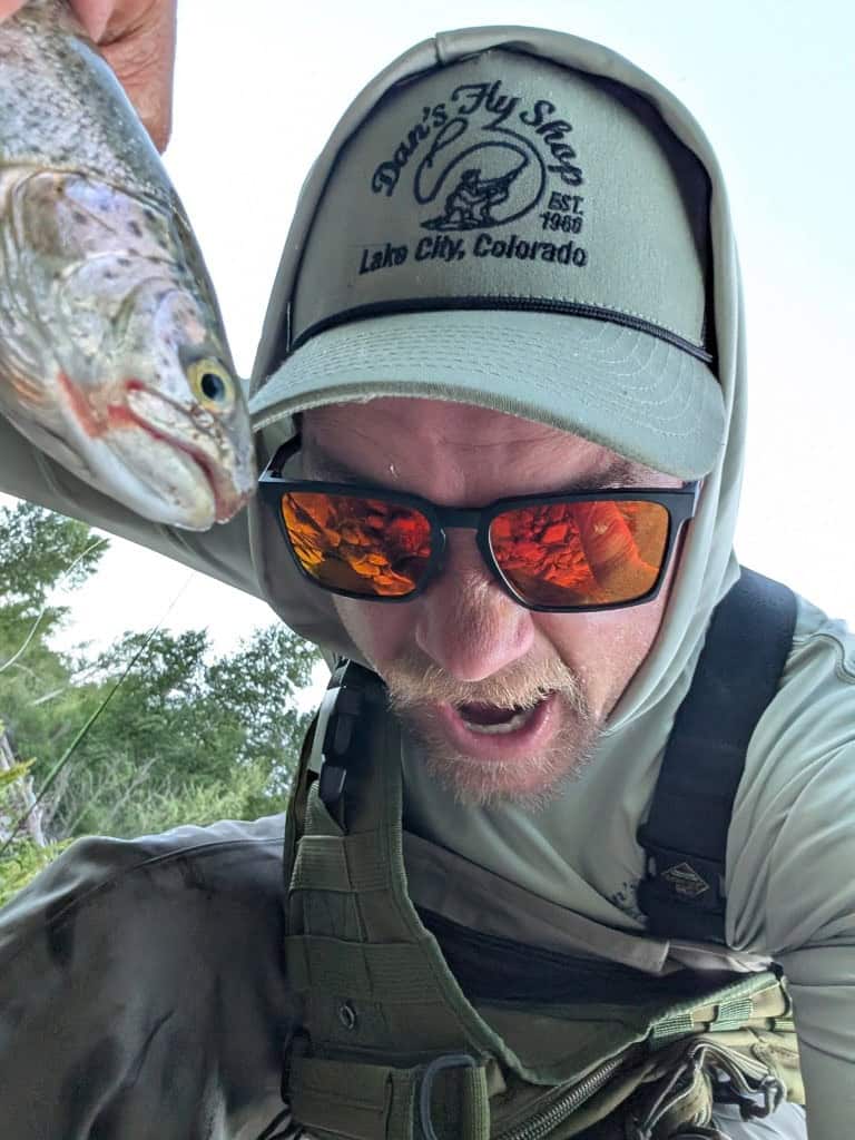 An angler wearing a DFS hat celebrates with a look of triumph while holding with a large trout.