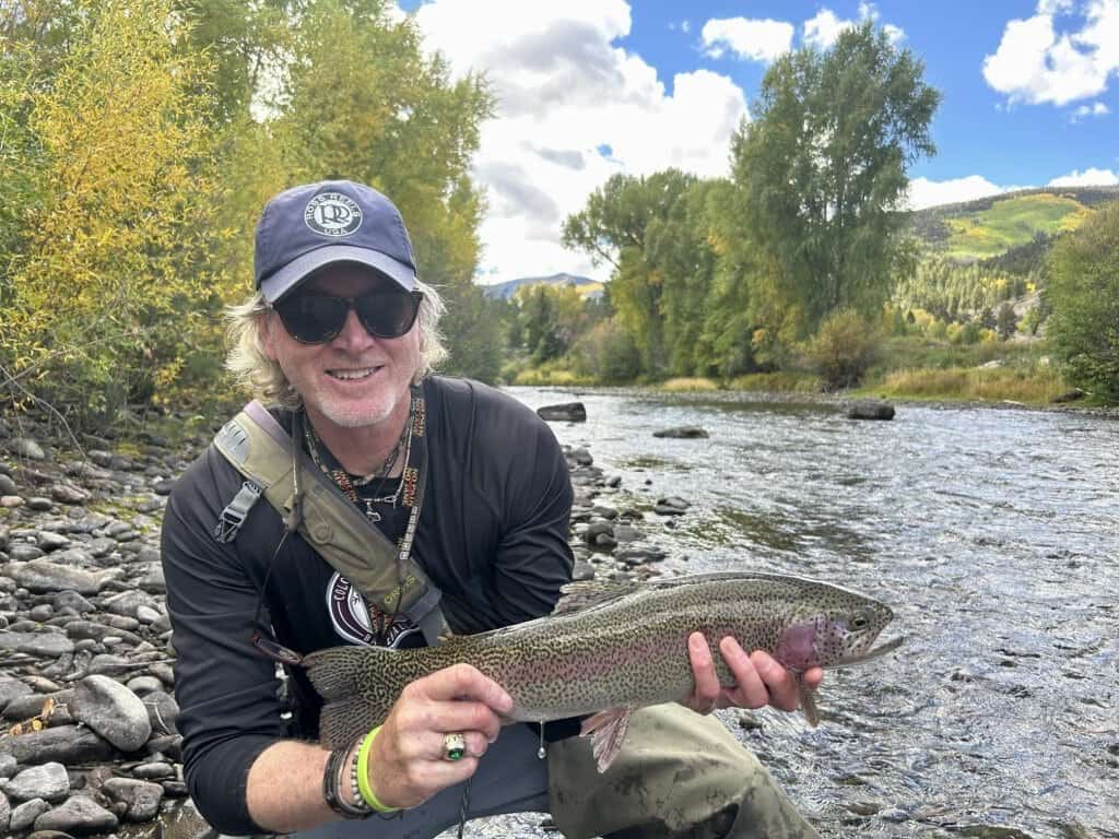 DFS guide shows off a huge rainbow trout beside a mountain river on private waters.