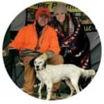 Mr. Millard in blaze orange smiles seated beside a woman in black and white dog.